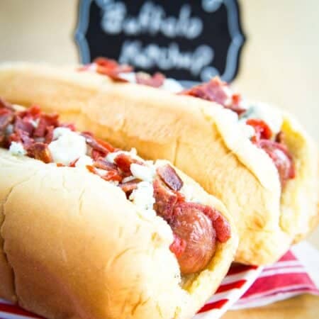 Closeup of a Buffalo Hot Dogs in a bun on a red and white striped plate.