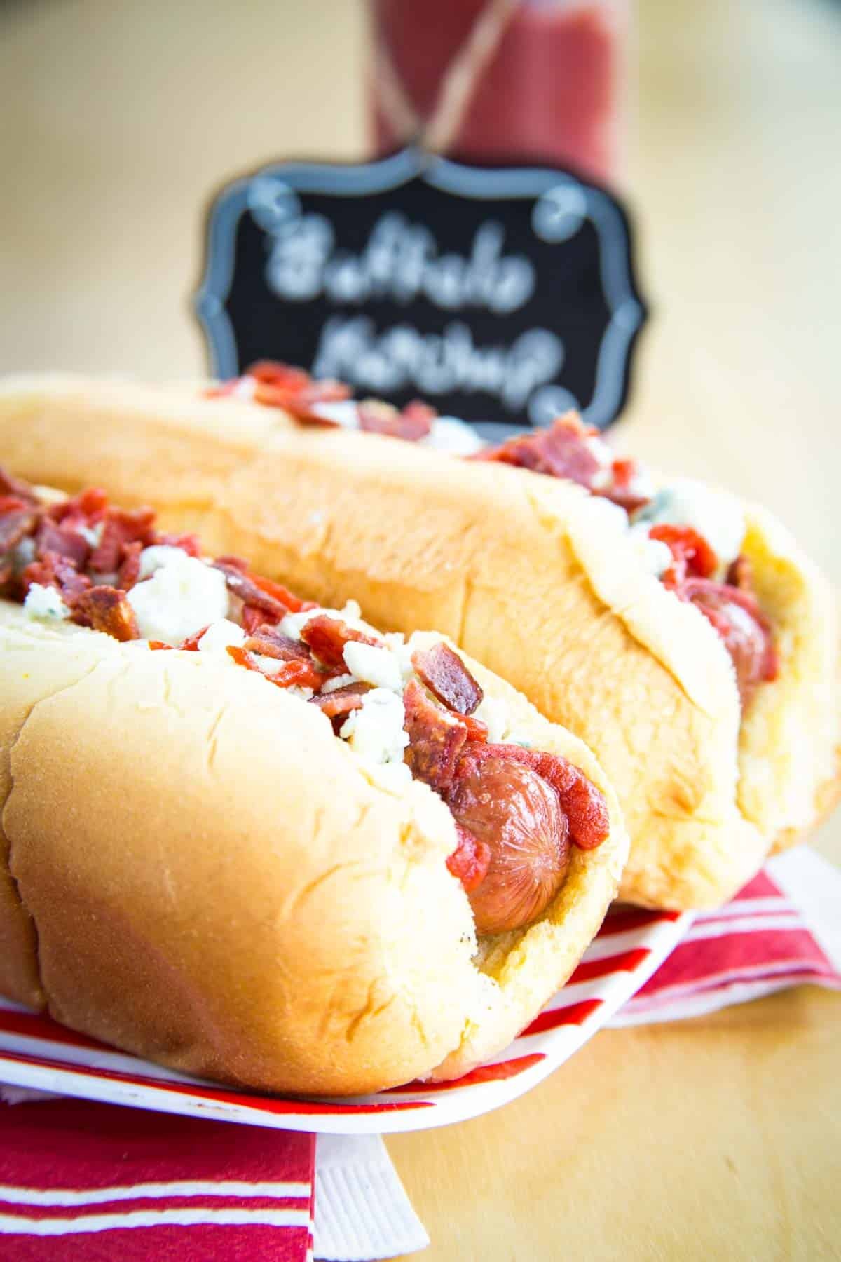 Closeup of a Buffalo Hot Dogs in a bun on a red and white striped plate.