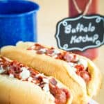 Two hot dogs in buns topped with bacon, blue cheese, and ketchup with text overlay that says "Buffalo Hot Dogs".