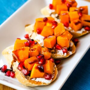Butternut Squash Goat Cheese Crostini garnished with pomegranate arils on a white plate.