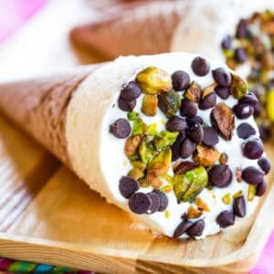 A closeup of a Cannoli Ice Cream Cone with mini chips and chopped pistachios on top.