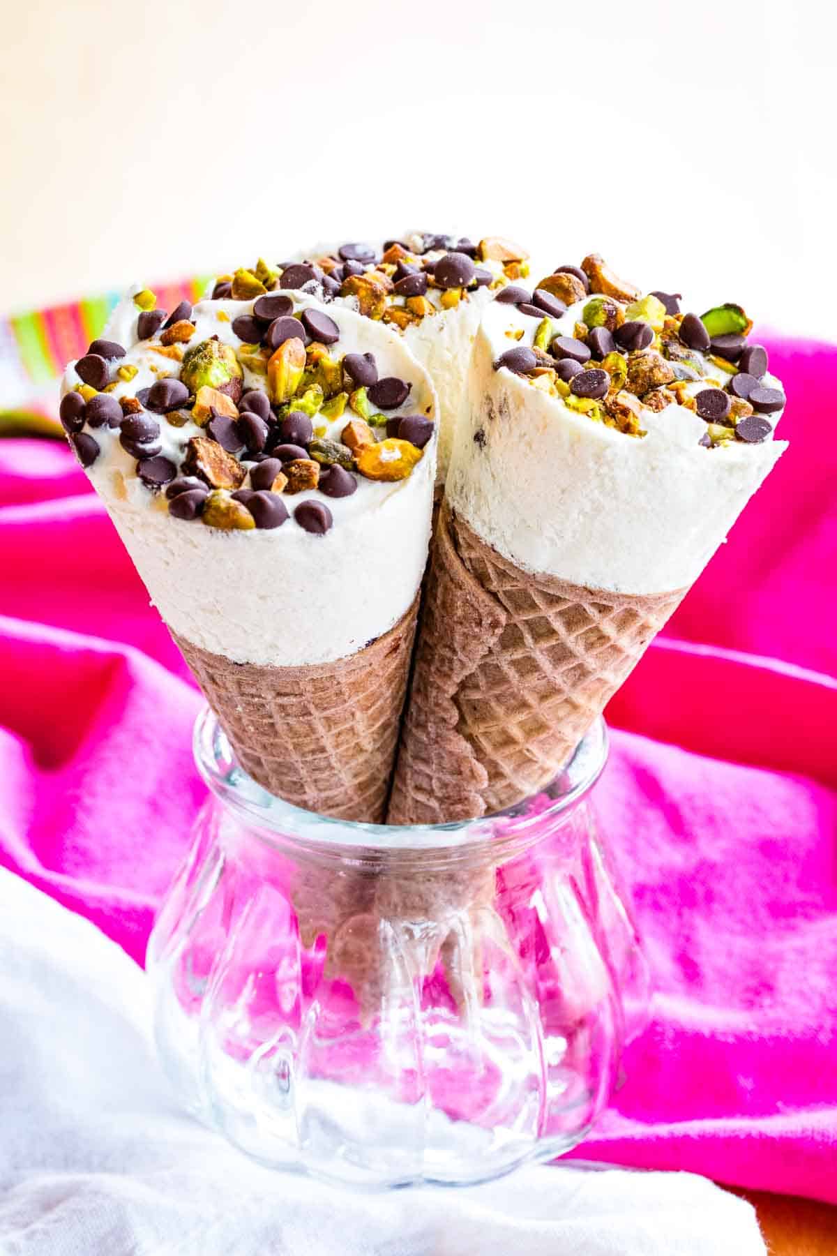 Three cannoli ice cream cones being held upright in a glass jar.