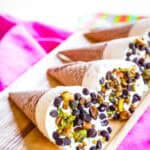 Four ice cream coned topped with chips and nuts laying on a wooden platter.