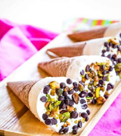 Four ice cream coned topped with chips and nuts laying on a wooden platter.