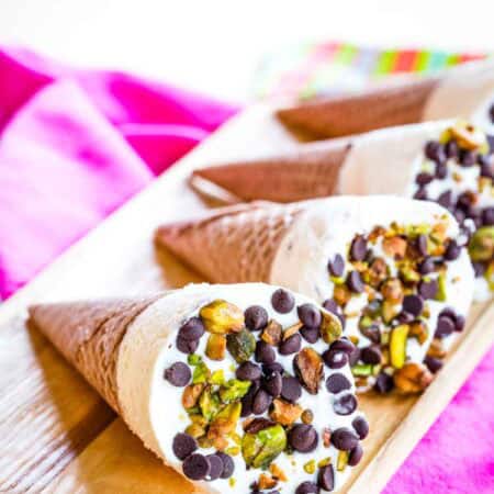 Four ice cream coned topped with chips and nuts laying on a wooden platter.