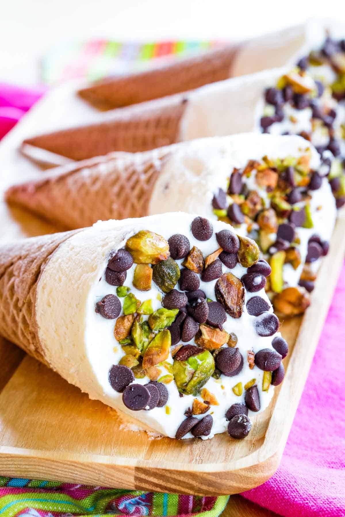 Cannoli ice cream cones lying on their sides on a wooden platter.