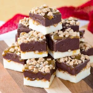 White and dark chocolate layered Caramel Toffee Fudge stacked in a pyramid on a wooden board.