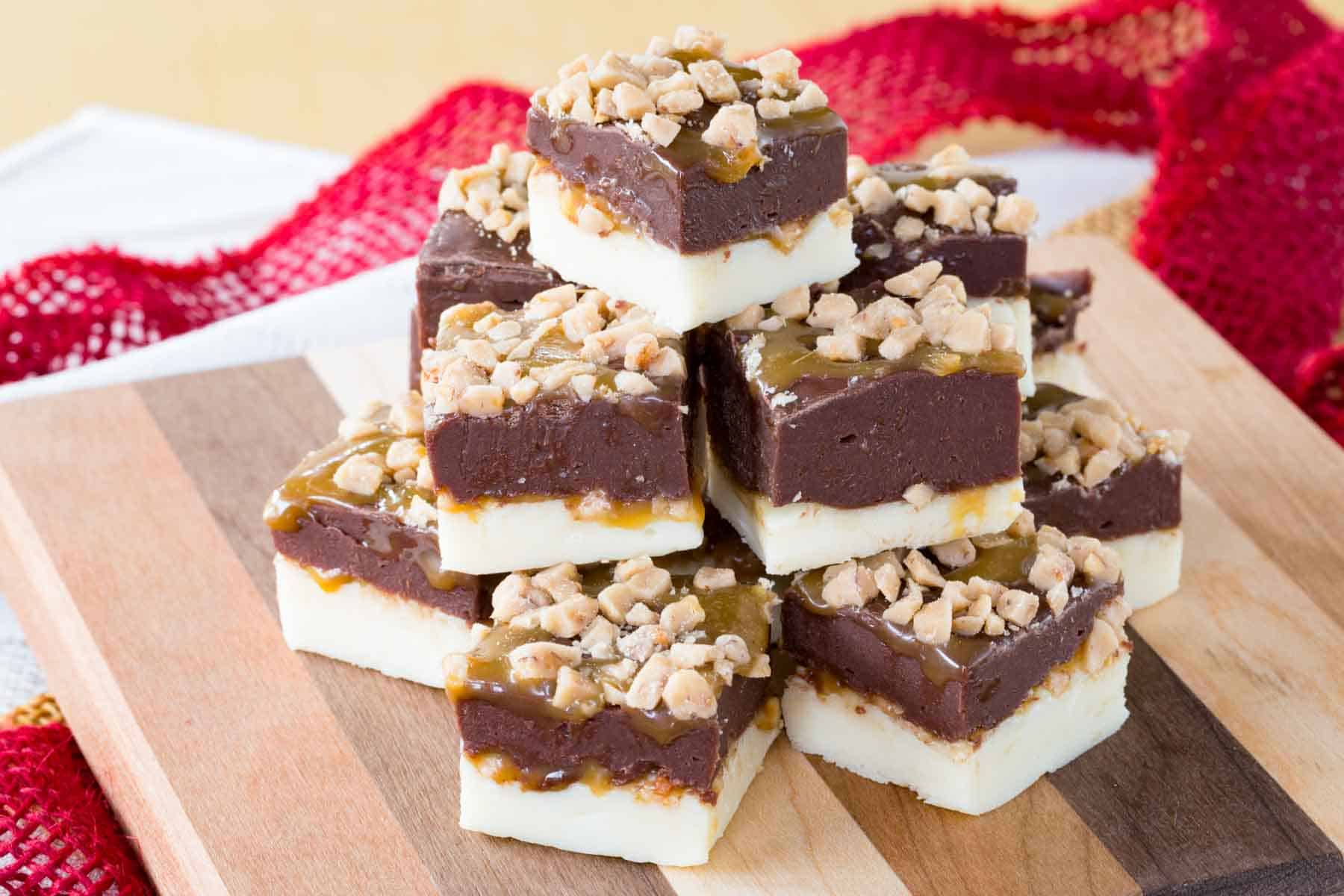 Caramel Toffee Fudge pieces stacked in a pyramid on a wooden board with red ribbon in the background.