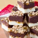 Squares of layered white and dark chocolate fudge on a wooden board with text overlay that says "Toffee Caramel Fudge".