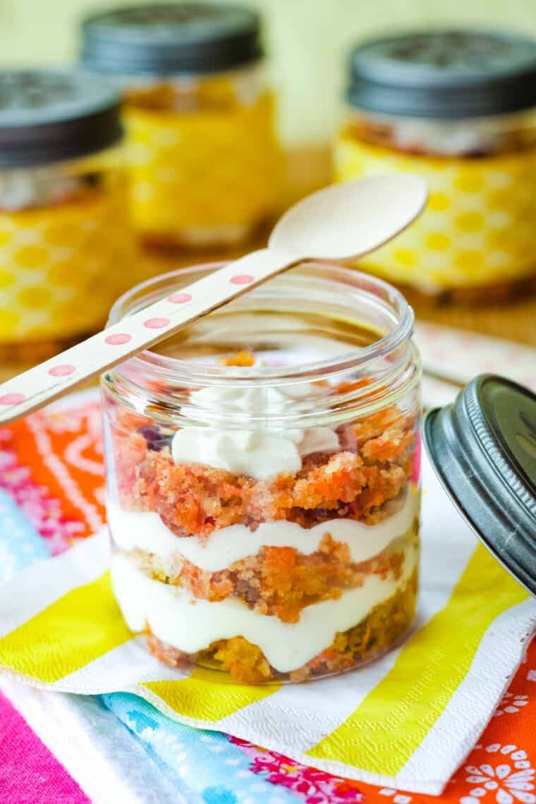 A carrot cake parfait in a jar with a wooden spoon resting on top of it.
