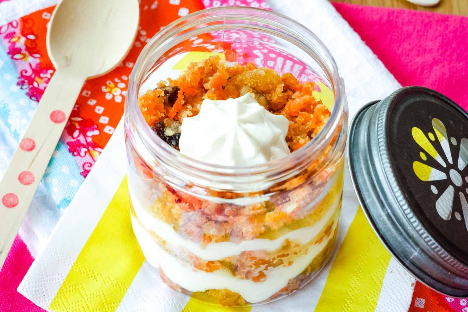 Looking down into a small jar of a carrot cake trifle with a lid leaning against it.
