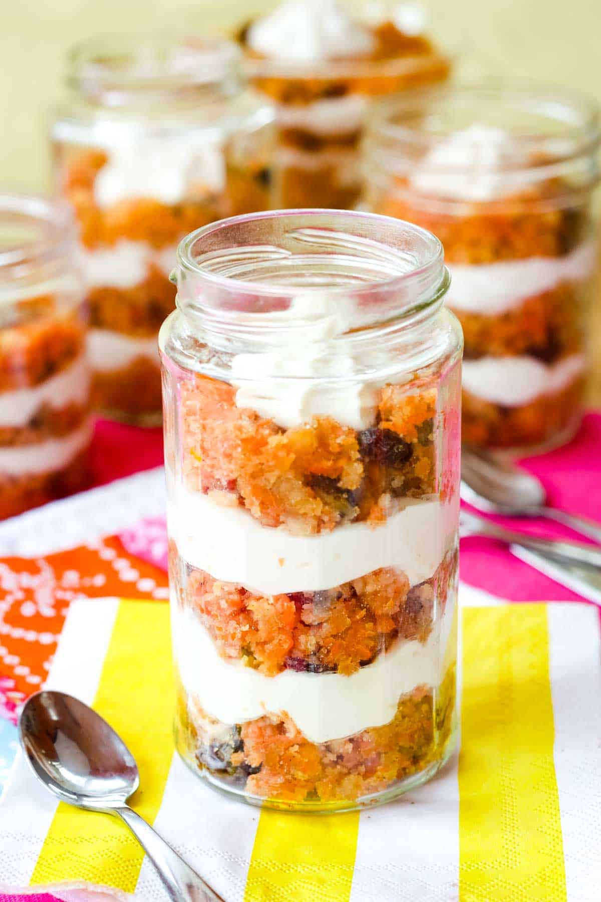 A carrot cake trifle in a jelly jar with more jars of parfaits in the background.