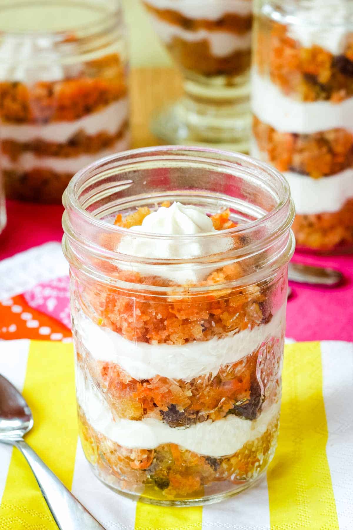 A small jelly jar with three layers of cake and cream cheese filling on a yellow and white striped napkin.