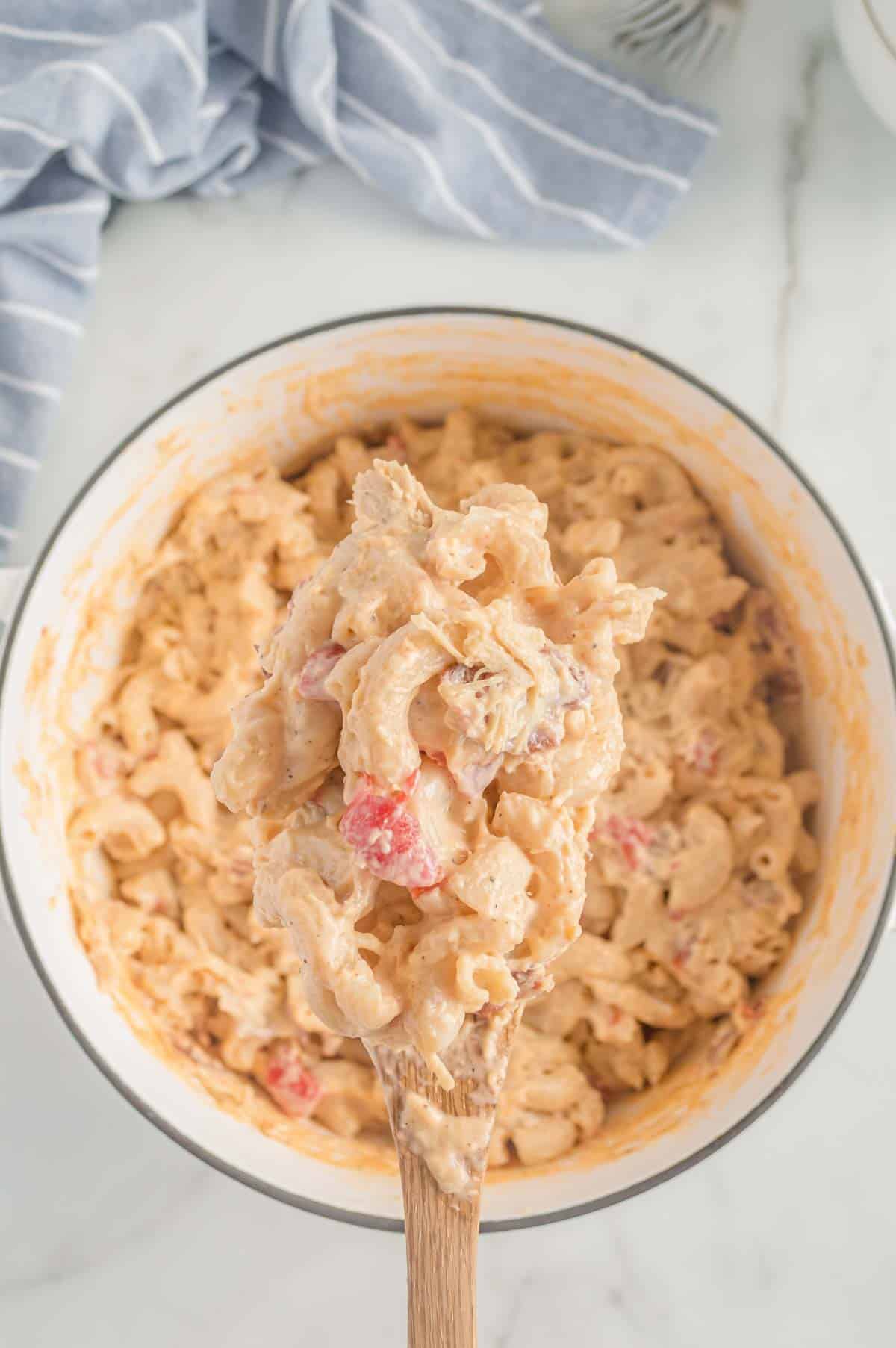 Chicken macaroni and cheese scooped up in a wooden spoon out of a pot.