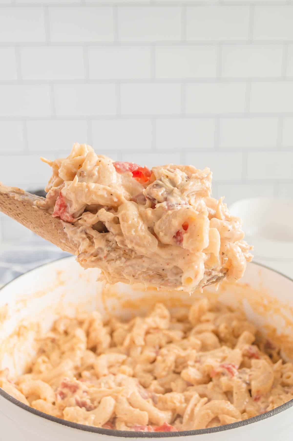 Scooping mac and cheese out of a pot with a wooden spoon.