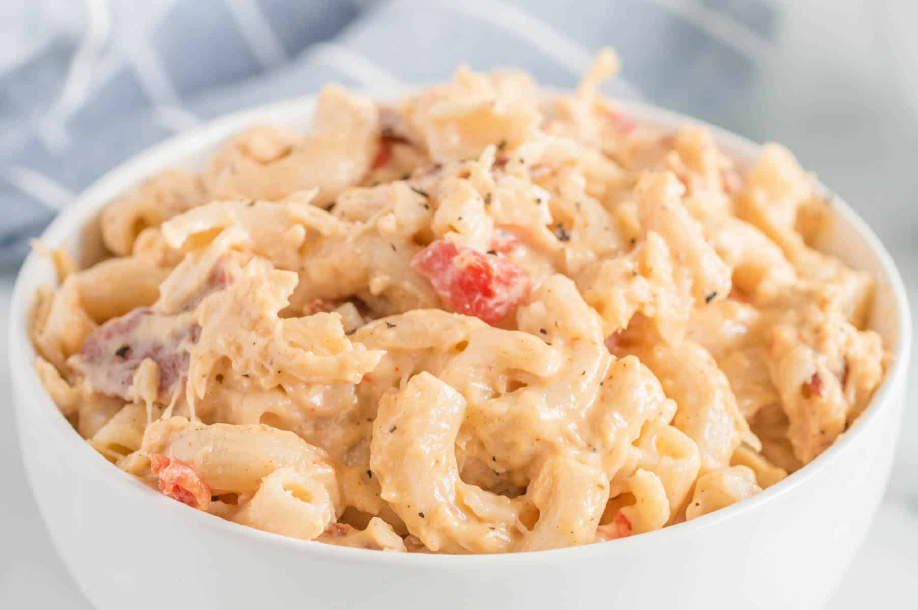 A closeup of a bowl of chicken mac and cheese with bacon and tomatoes served in a white bowl.