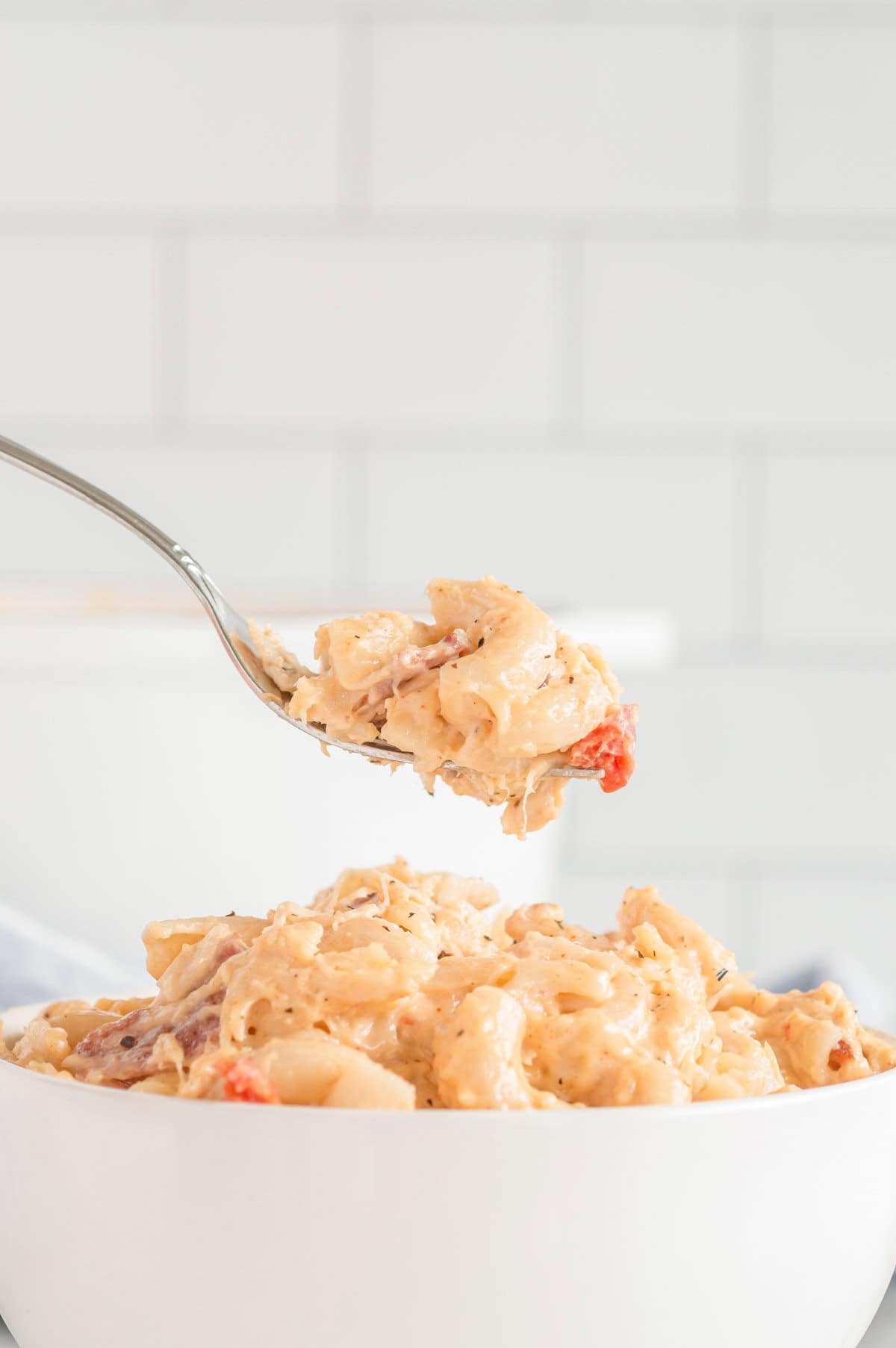 A bite of macaroni and cheese on a fork over a bowl.