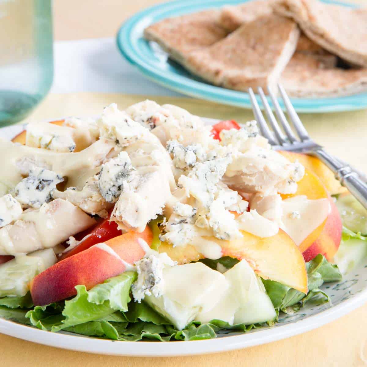 A chicken peach salad with tomatoes, blue cheese, and dressing on a white plate.