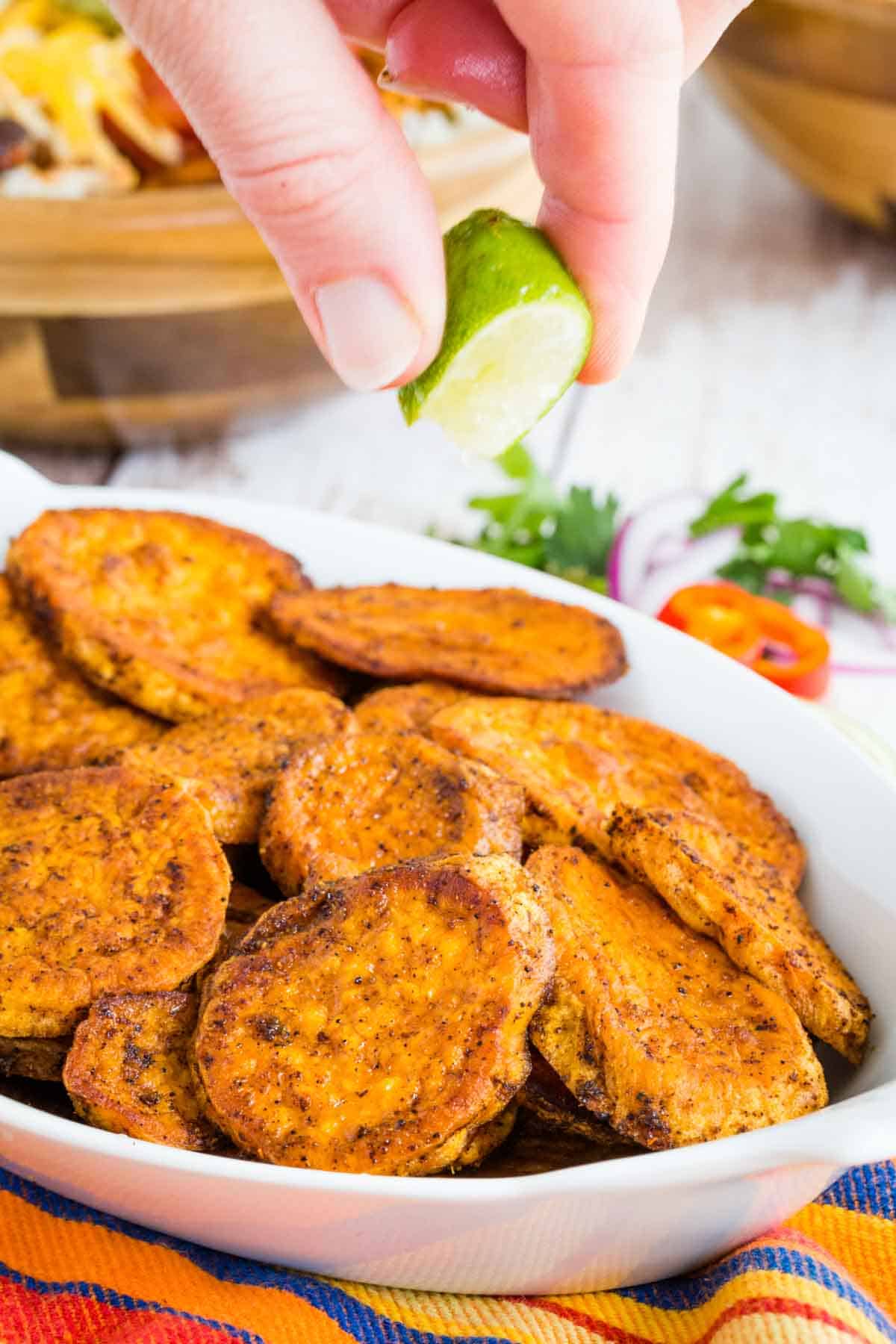 Squeezing a lime over baked sweet potato slices.