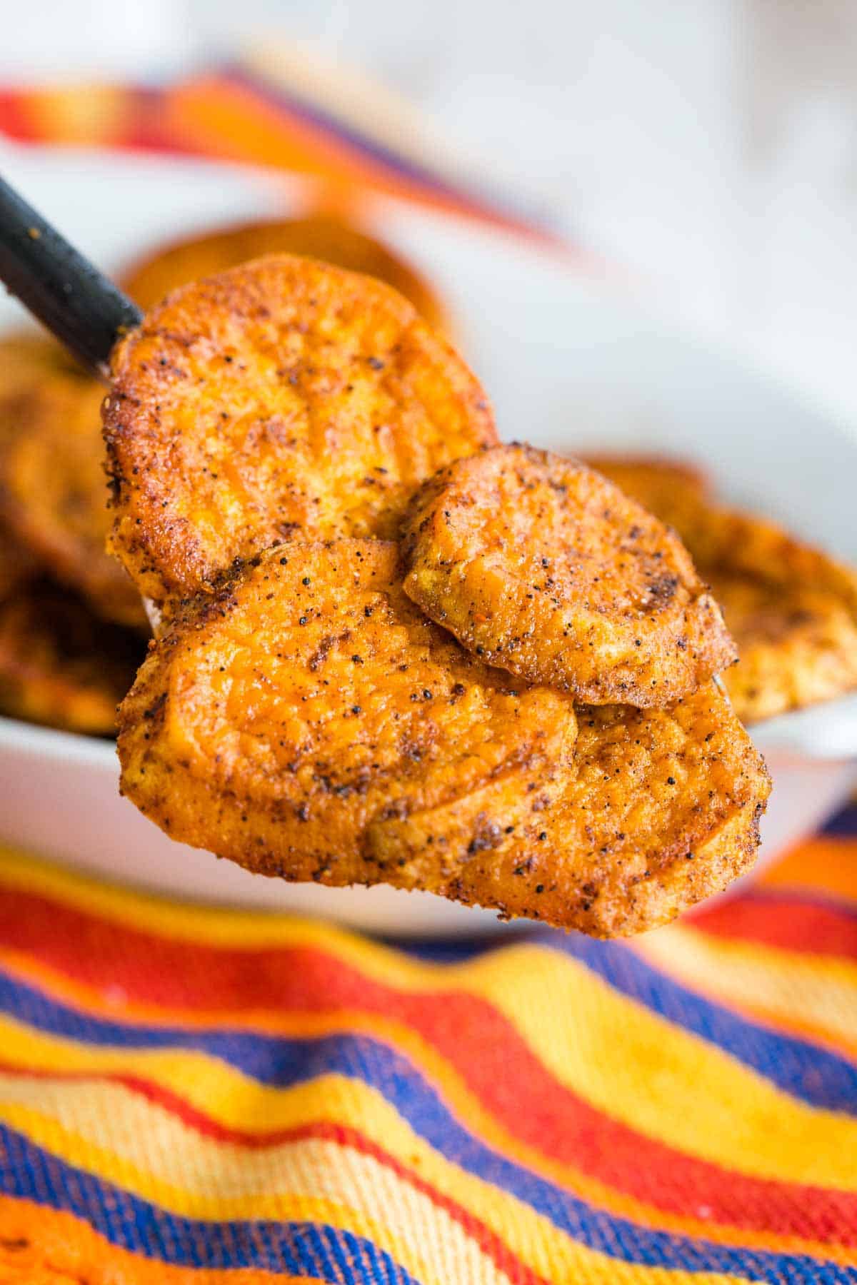 A serving spoon holding baked sweet potato slices coated in spices.