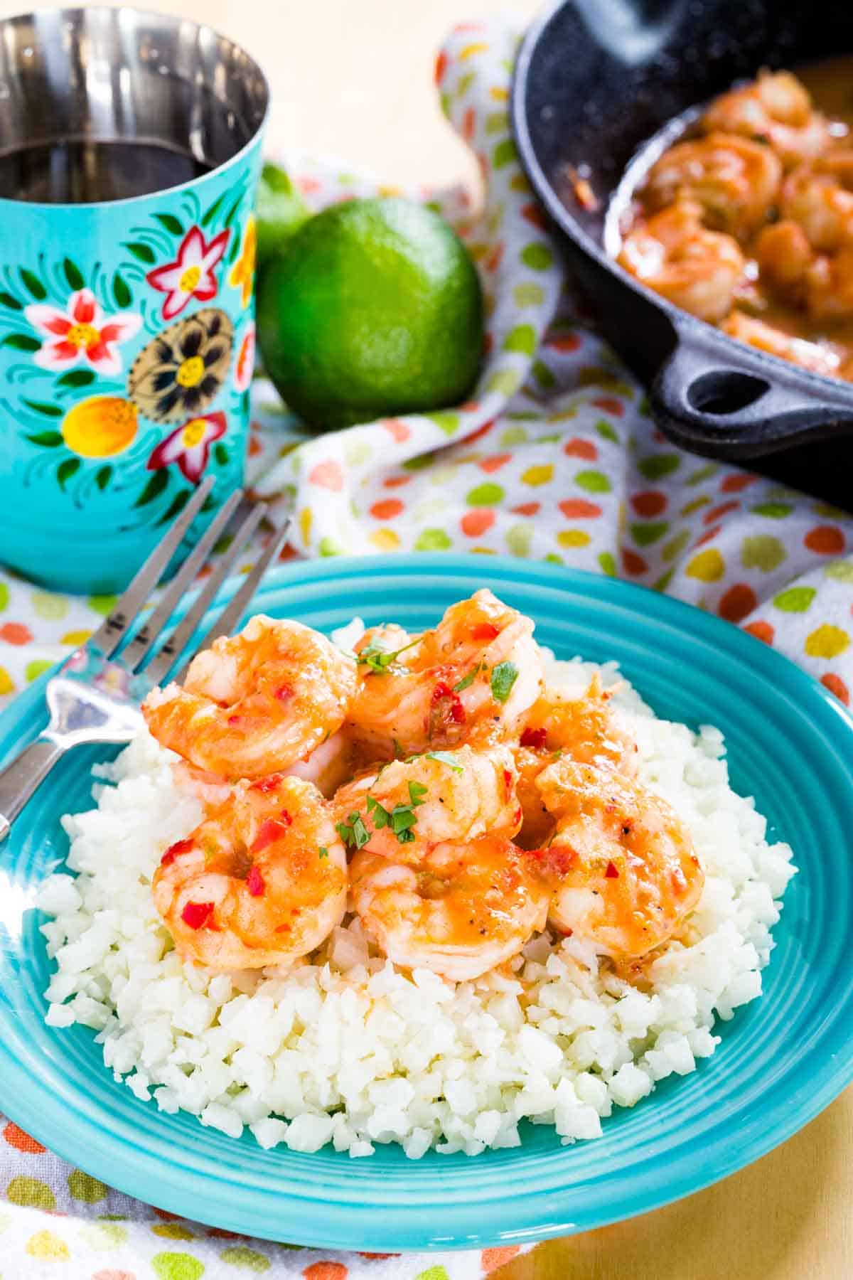 Chili Lime Shrimp Served with Cauliflower Rice with a turquoise cup of water and a skillet of the shrimp behind it.