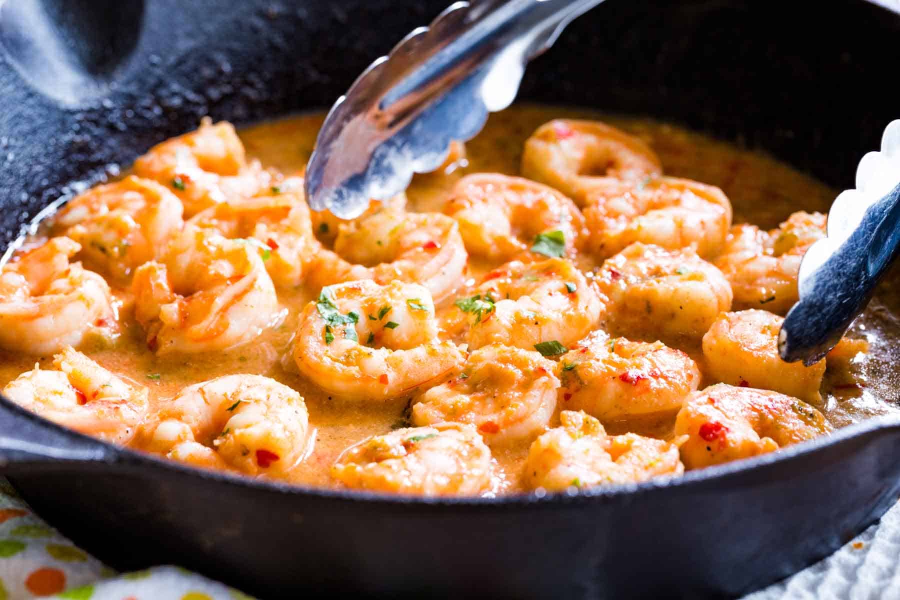 Chili Lime Shrimp with tongs in a cast iron skillet.