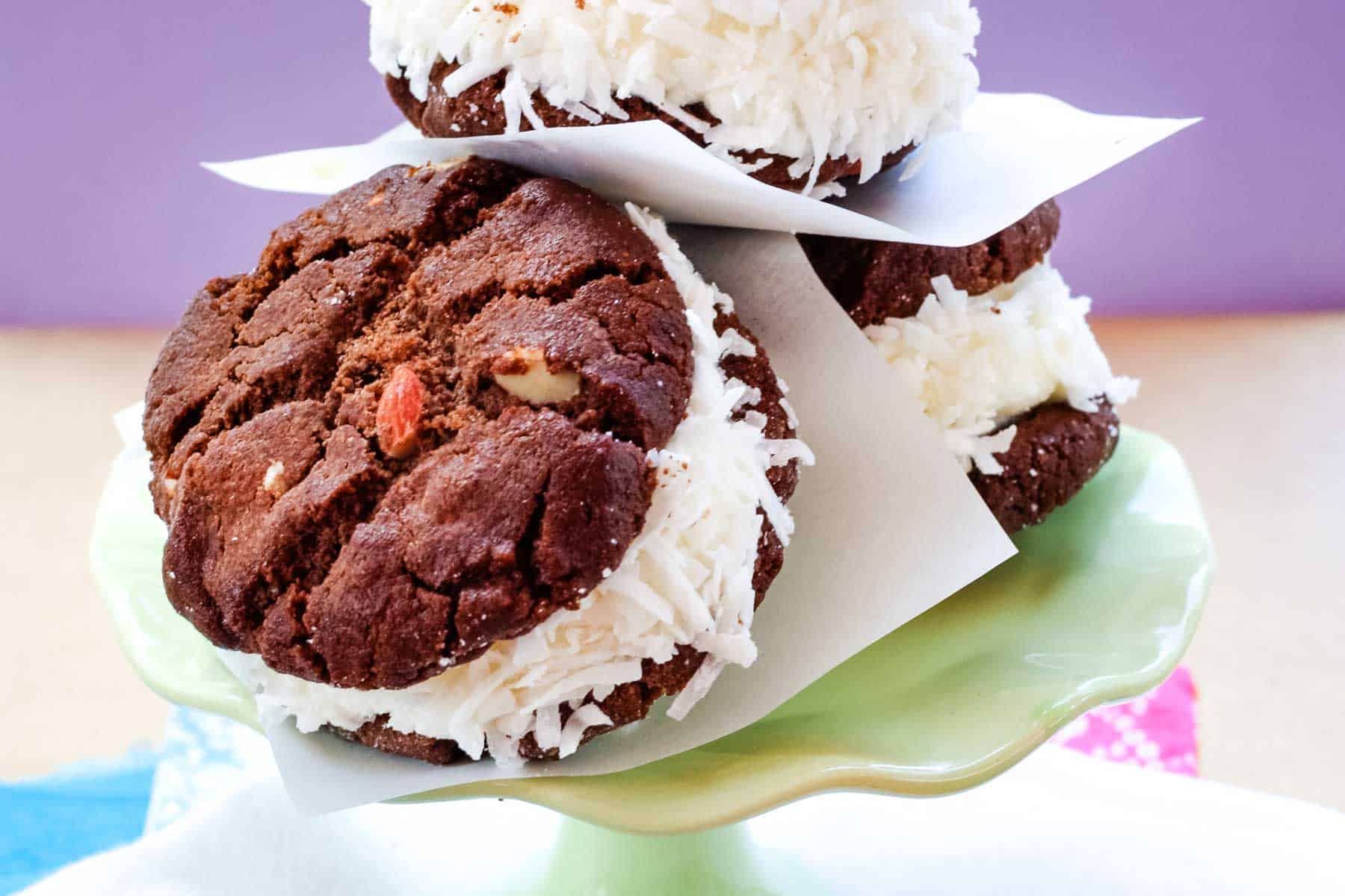 A closeup of a chocolate coconut ice cream sandwich leaning against some other ones on a small stand.