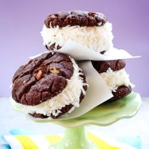 Three ice cream sandwiches made with coconut gelato and two chocolate almond cookies leaning against each other on a small green cake stand.