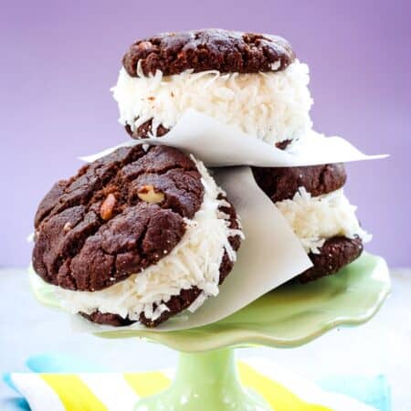Three ice cream sandwiches made with coconut gelato and two chocolate almond cookies leaning against each other on a small green cake stand.