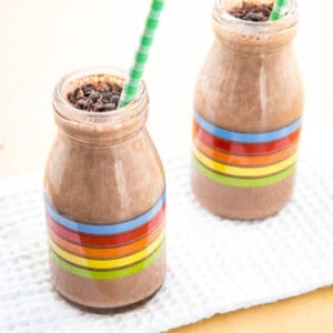 Two chocolate smoothies with cacao nibs floating on top in glass bottles with rainbow stripes.