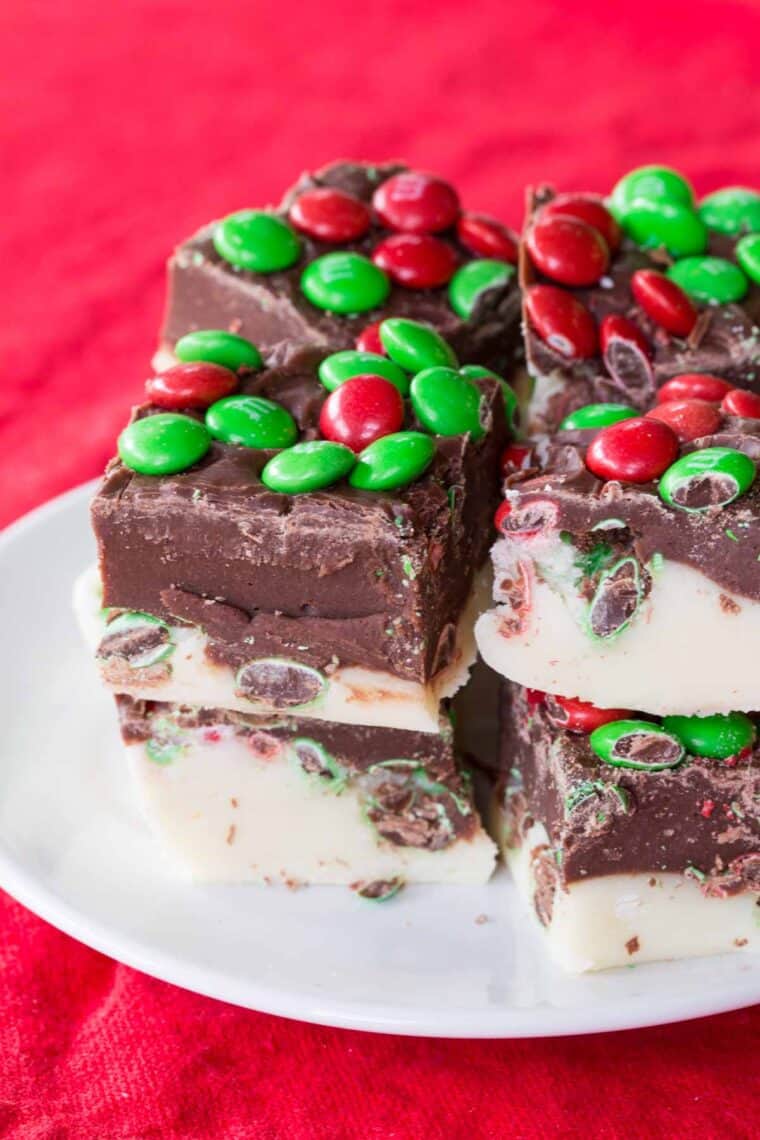 Two layer fudge with red and green M&M's candies in it on a white plate on top of a red napkin.