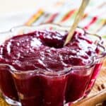 Cranberry sauce in a scalloped glass bowl with a spoon with text overlay that says "Cinnamon Orange Cranberry Sauce".