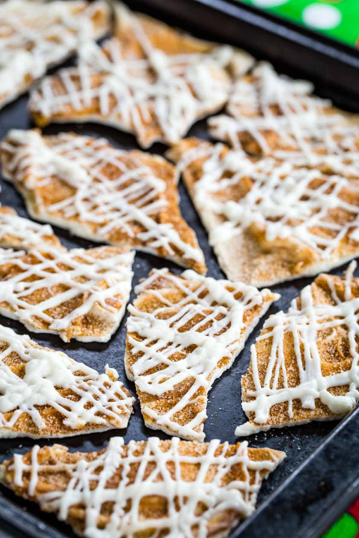 A closeup of white chocolate bark pieces topped with Cinnamon Sugar on a blackened sheet pan.