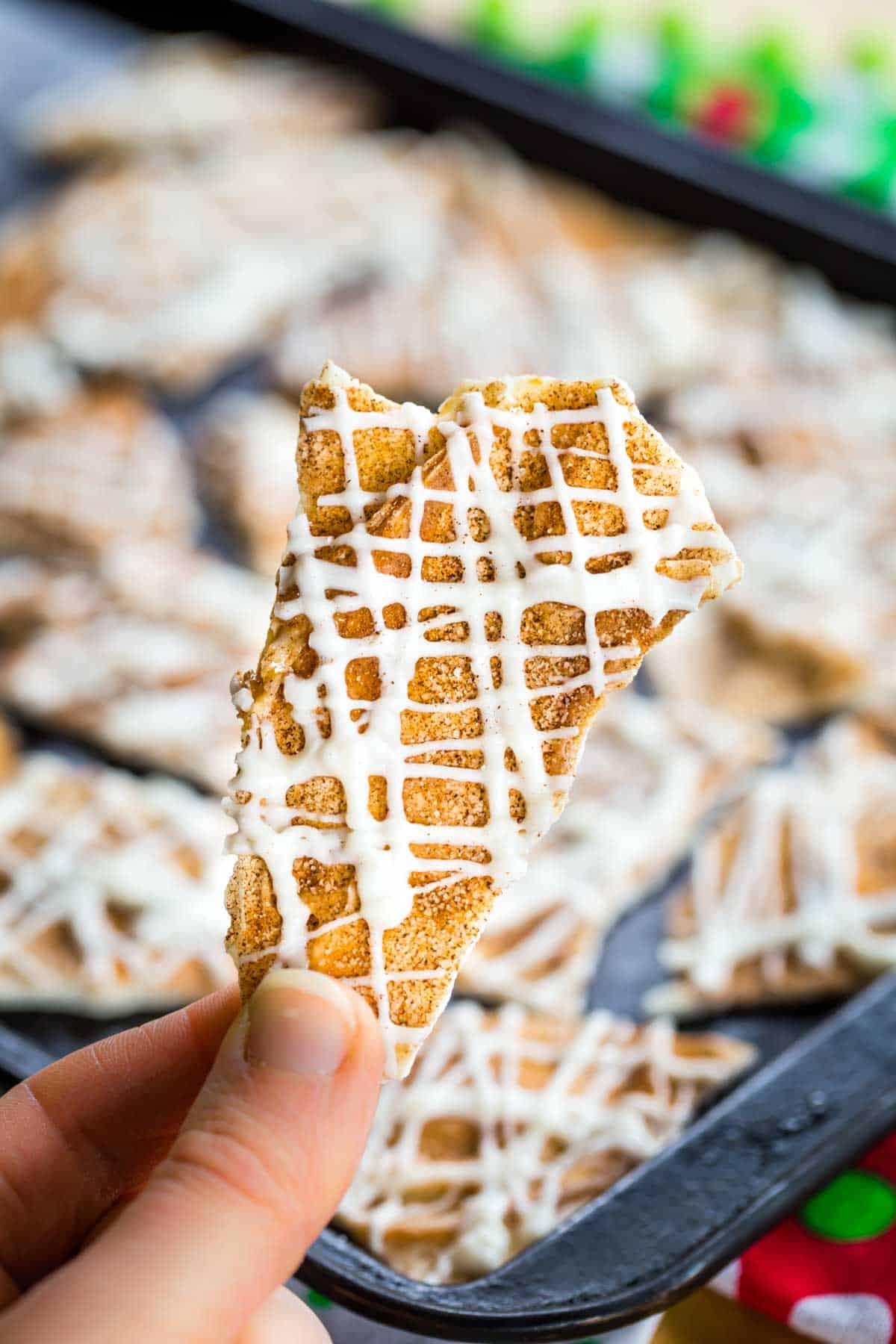 Fingers holding a piece of White Chocolate Bark topped with cinnamon-sugar and a drizzle of more white chocolate.