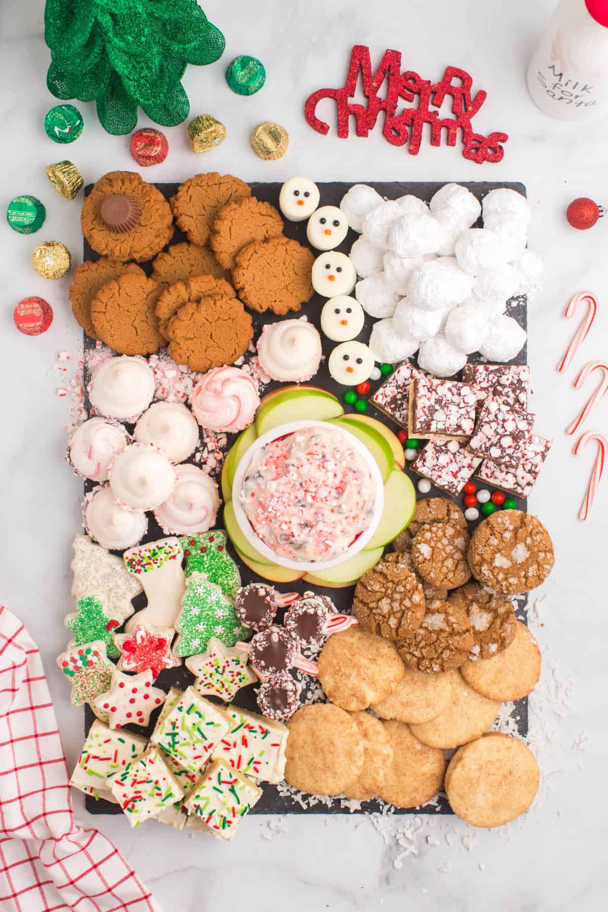 Looking down at a cookie charcuterie board on a slate platter with piles of different gluten free cookies and candies with a bowl of candy cane cheesecake dip in the middle.
