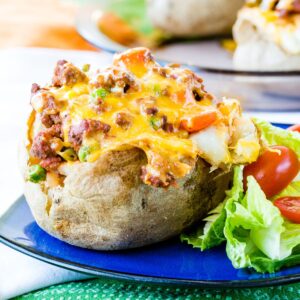A cottage pie baked potato on a blue plate with salad.
