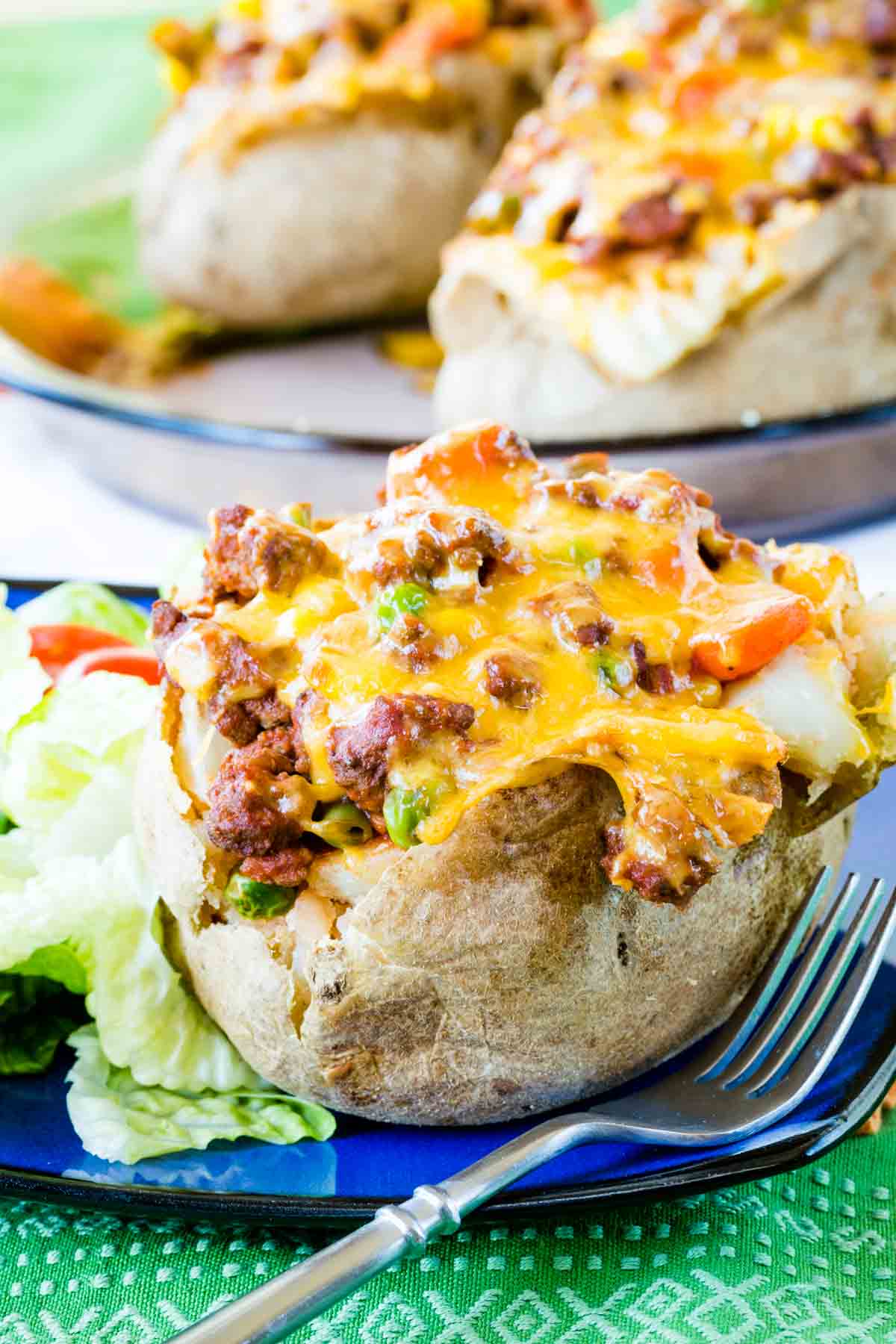 A cottage pie baked potato on a blue plate with a fork and more stuffed baked potatoes in a baking dish in the background.