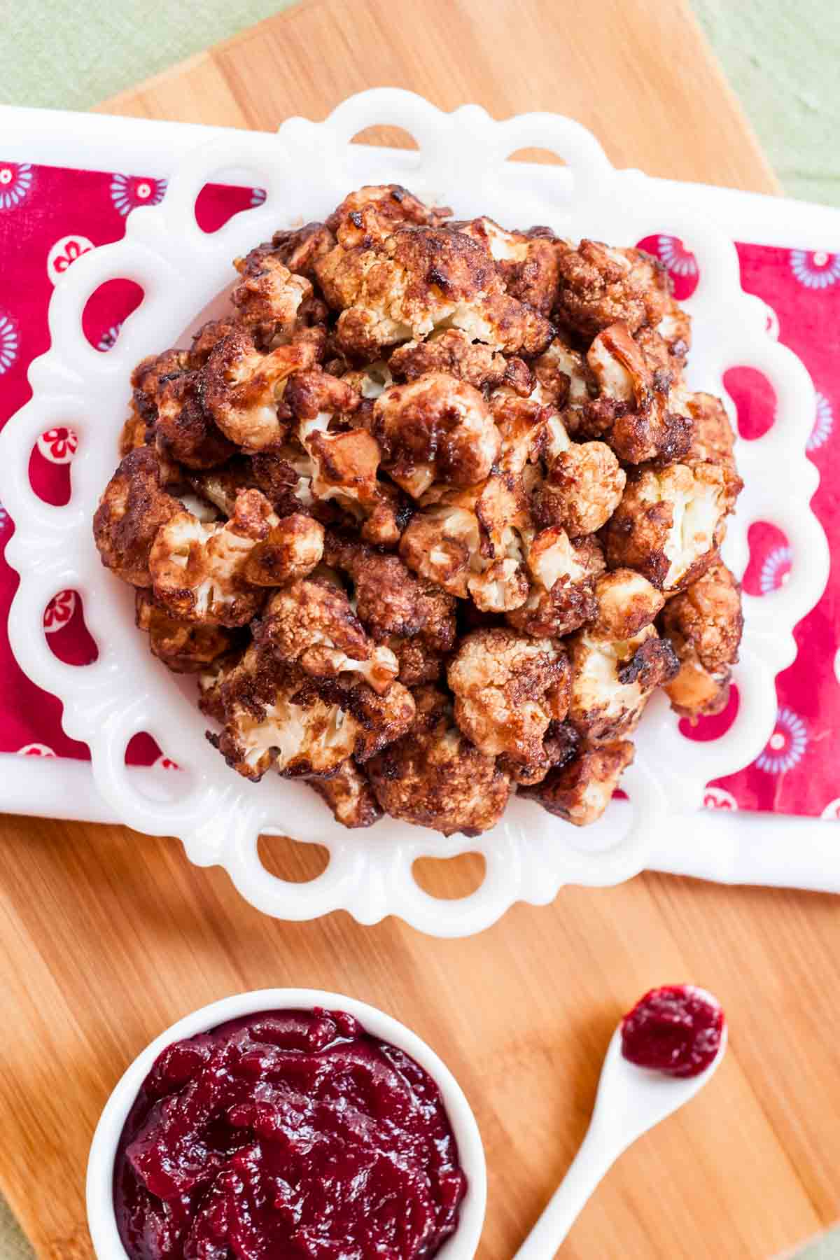 Overhead of a plate of cranberry balsamic cauliflower bites next to a bowl of cranberry sauce.