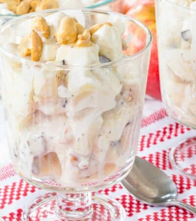 Apple Candy Bar Salad in a glass pedestal dish on top of a red and white checked napkin.