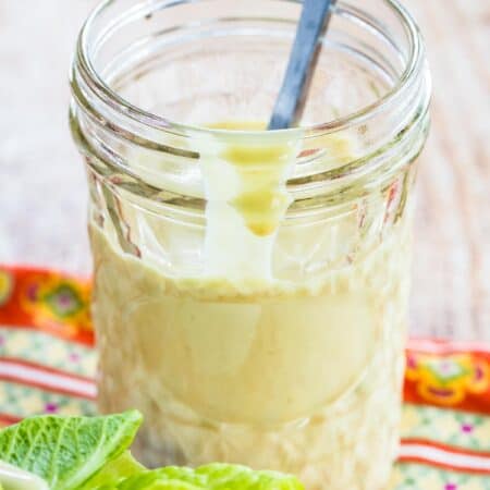 Creamy Maple Dijon Greek Yogurt Dressing in a glass jar with a spoon.