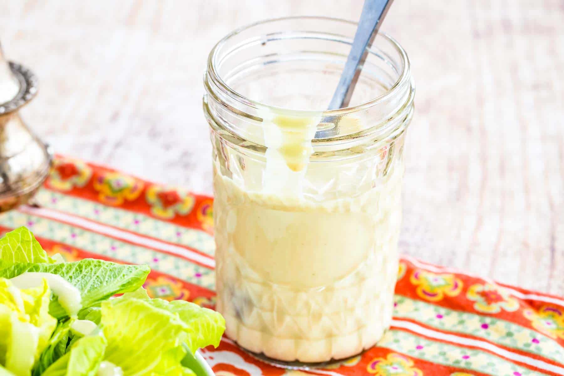 A glass mason jar with Creamy Maple Dijon Dressing on a colorful placemat.