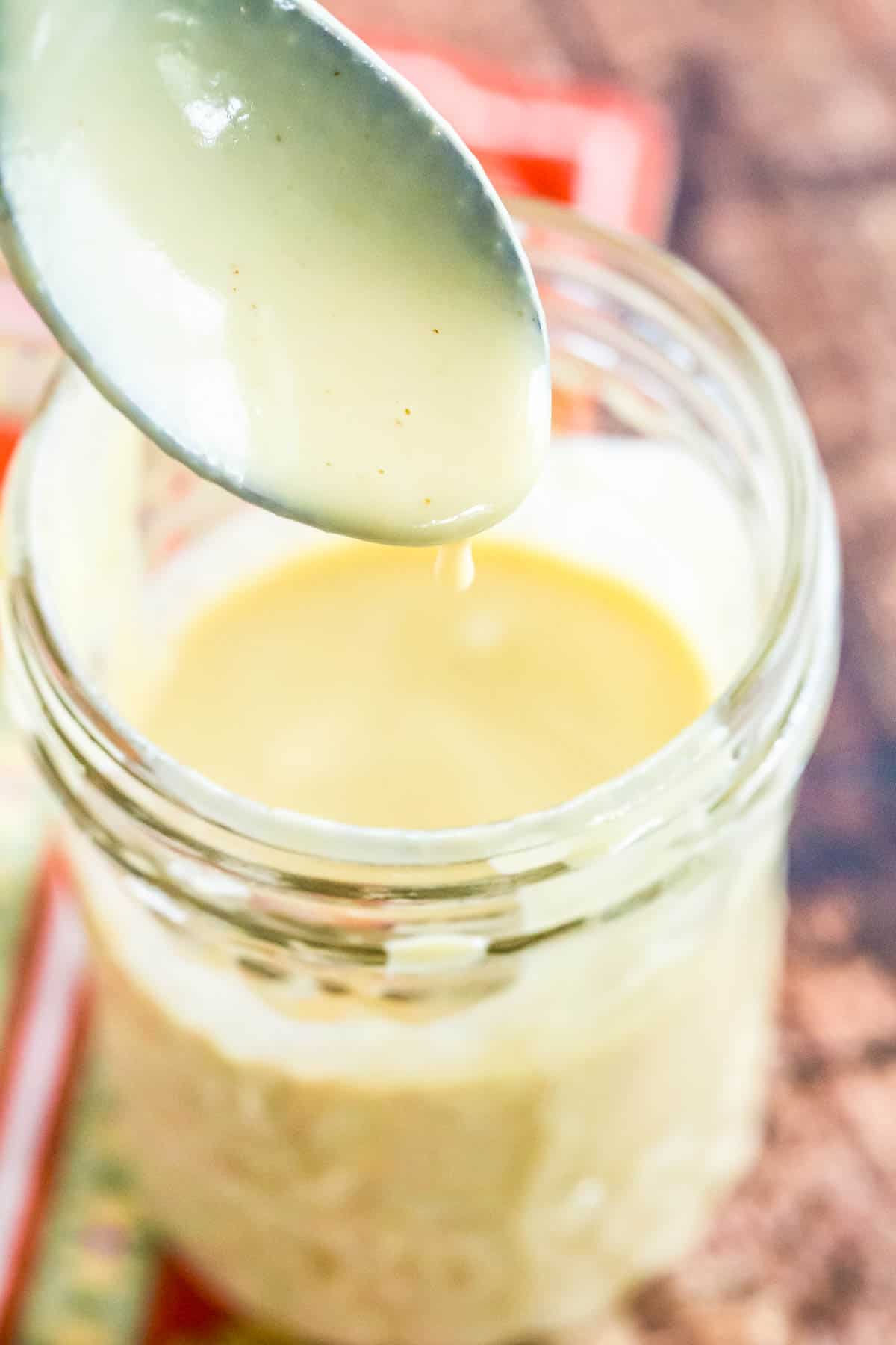 Maple Dijon dressing dripping off a spoon into a jar.