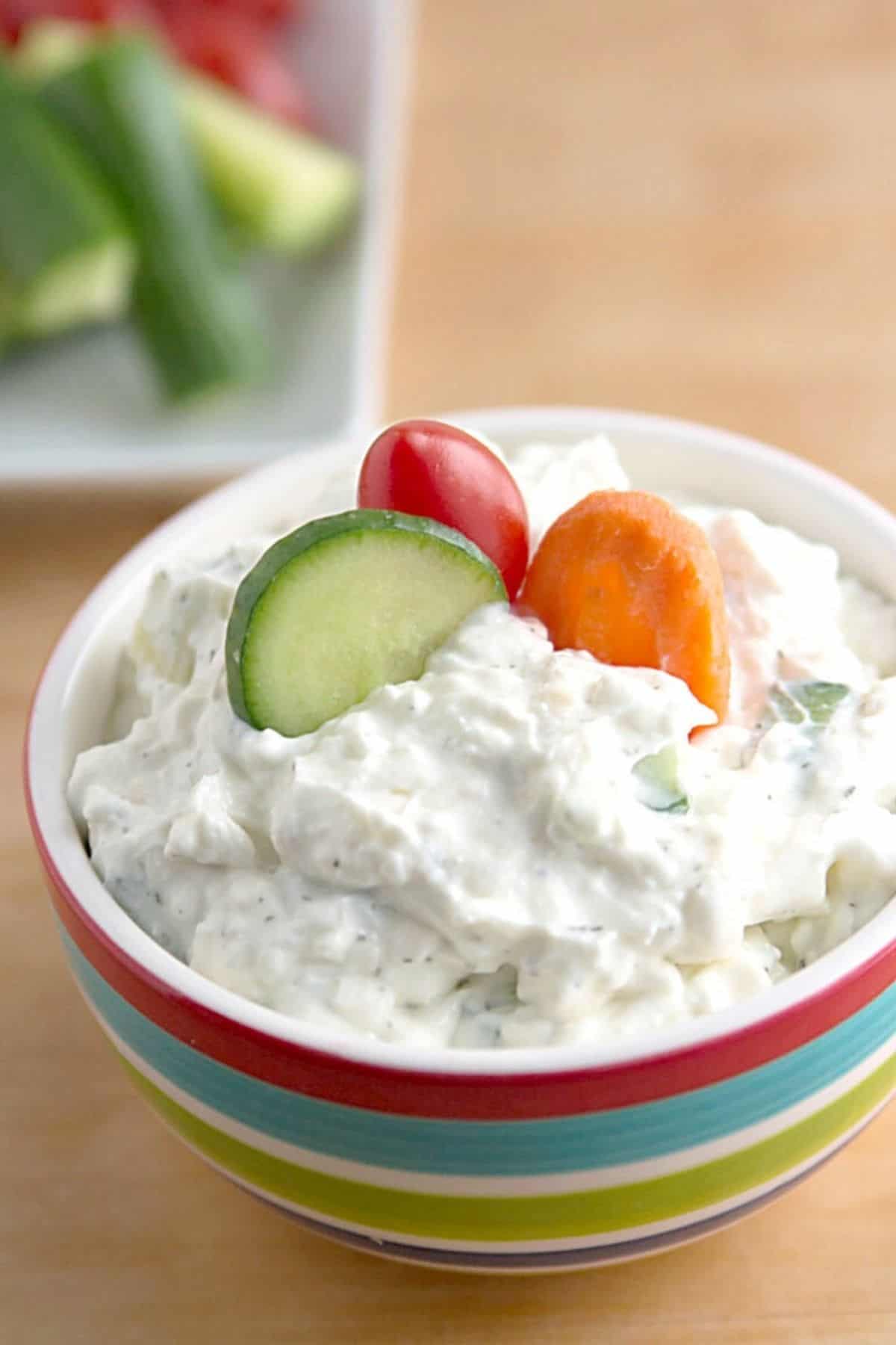 Creamy cucumber dill dip in a striped bowl with a few raw veggies placed in the top.