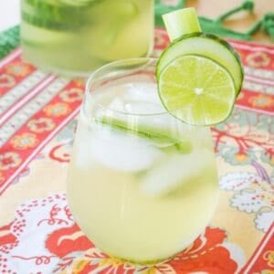 A white wine cocktail in a stemless wine glass with cucumber and lime slices on the rim.