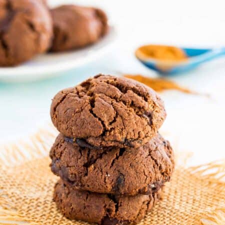 A stack of three Mexican chocolate cookies filed with chocolate chunks on a piece of burlap.
