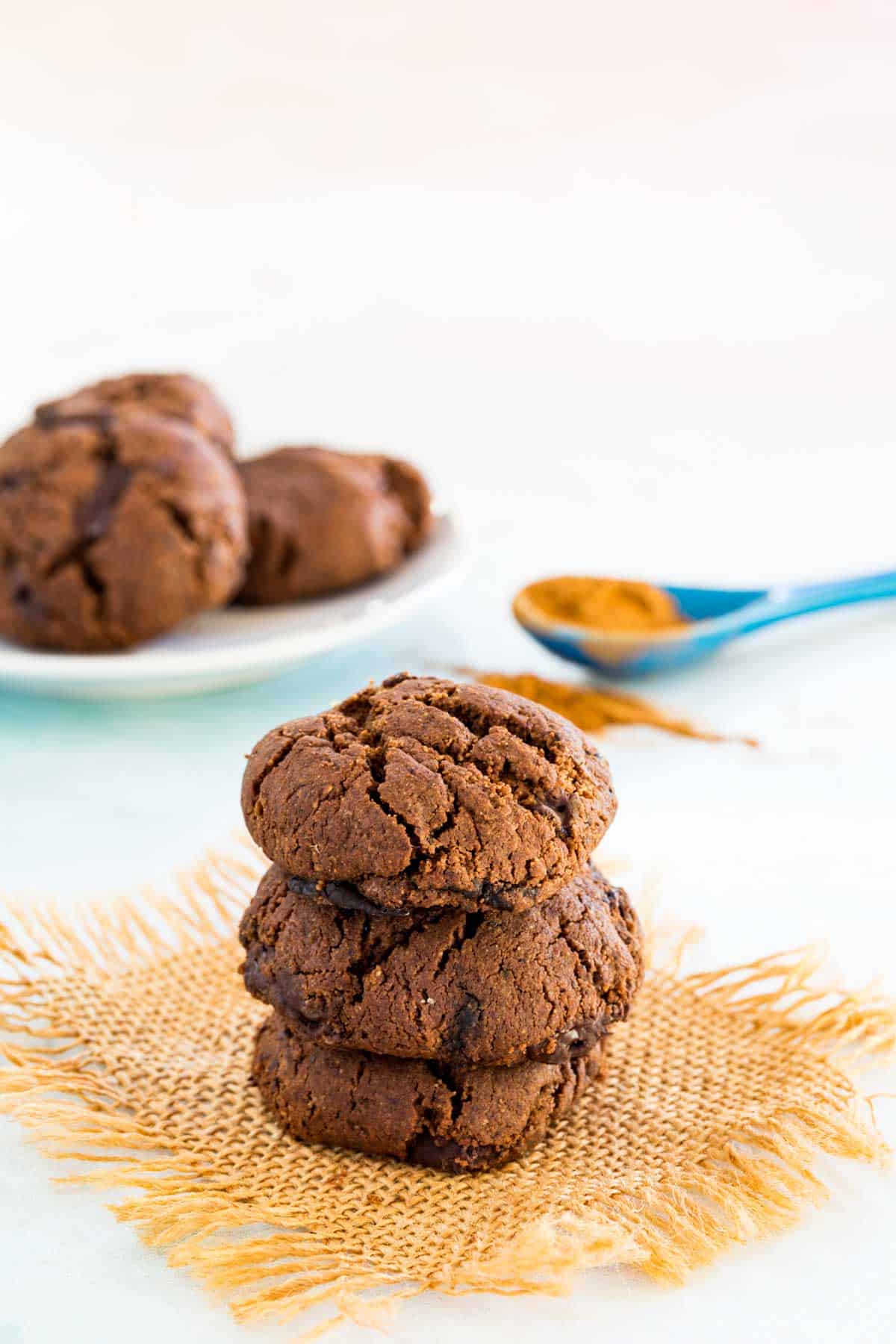 Three Flourless Mexican Hot Chocolate Cookies on top of each other on a piece of burlap with three more on a plate in the background.