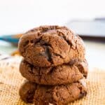 A stack of three chocolate chunk cookies on a piece of burlap with text overlay that says "Flourless Mexican Hot Chocolate Cookies".
