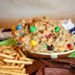 A football-shaped dough of edible monster cookies dough on a plate with pretzel sticks and chocolate tortilla chips.