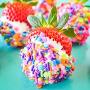White chocolate covered strawberries with rainbow sprinkles on them.