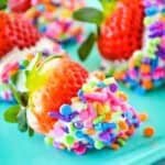 White chocolate dipped strawberries covered in rainbow sprinkles on a turquoise plate.